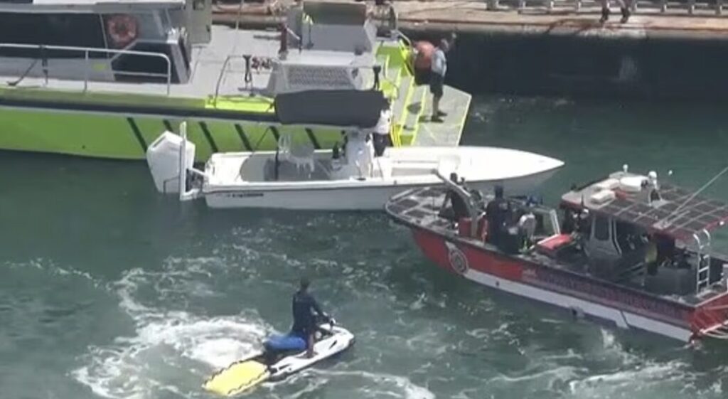 Rescue teams on boats and personal watercraft conduct search operations in Biscayne Bay after a sailboat sinks off Hibiscus Island in Miami Beach, with a rescuer towing a yellow board.